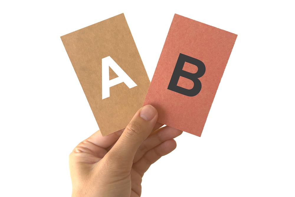 AとBと書かれたカードを持つ手